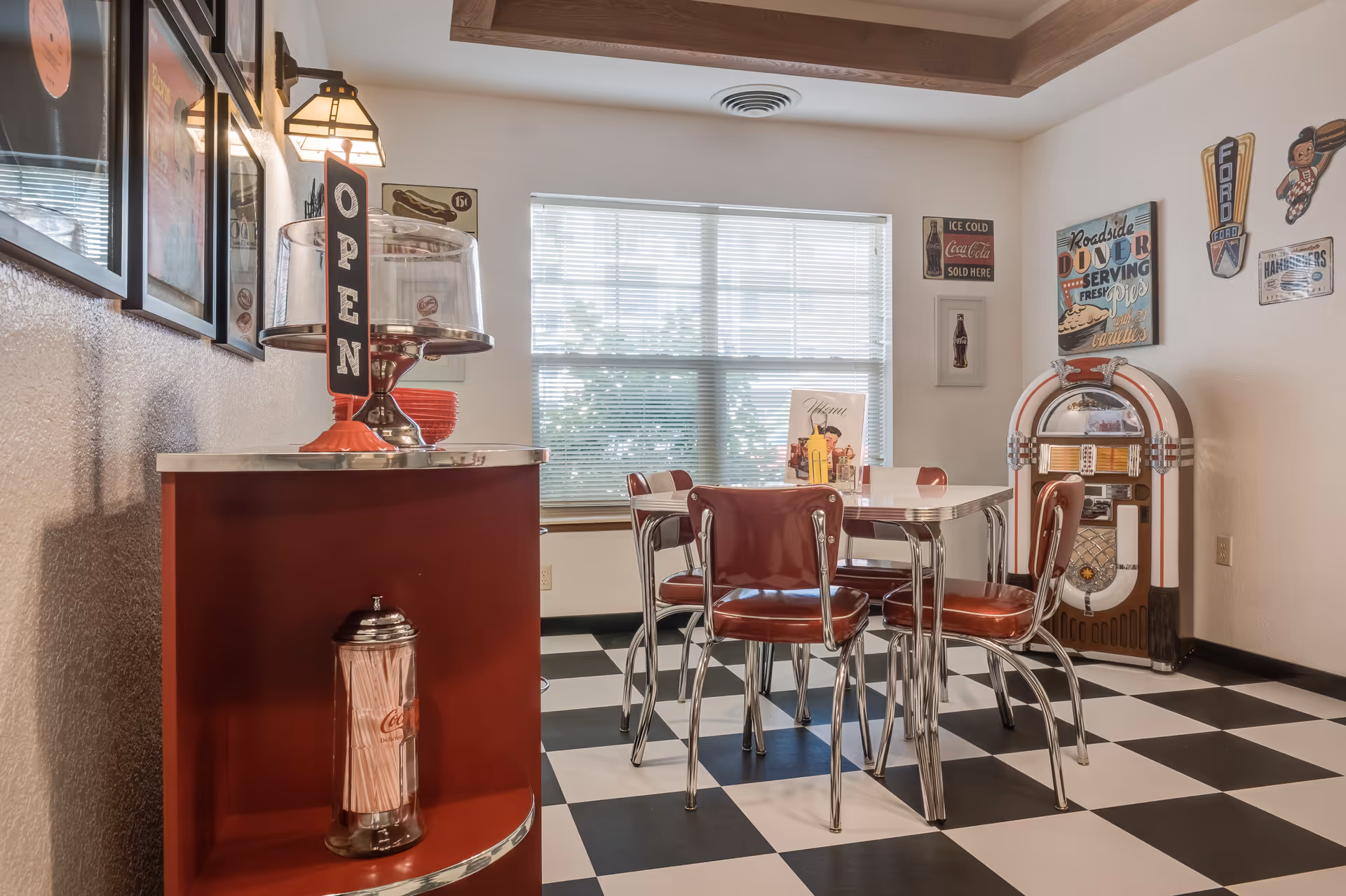 Retro diner-style dining area with red vinyl chairs, a checkerboard floor, a counter with an 'OPEN' sign, and a jukebox.