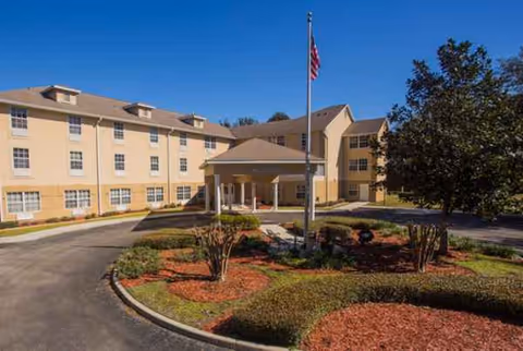 Exterior view of Highland Place senior living facility with entrance, flagpole, and manicured landscaping.