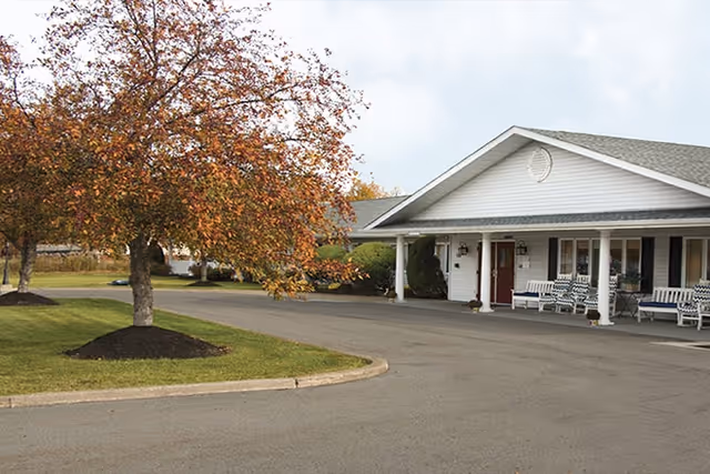 Exterior view of Elderwood Village at St. Gregory Court with a porch and autumn trees.
