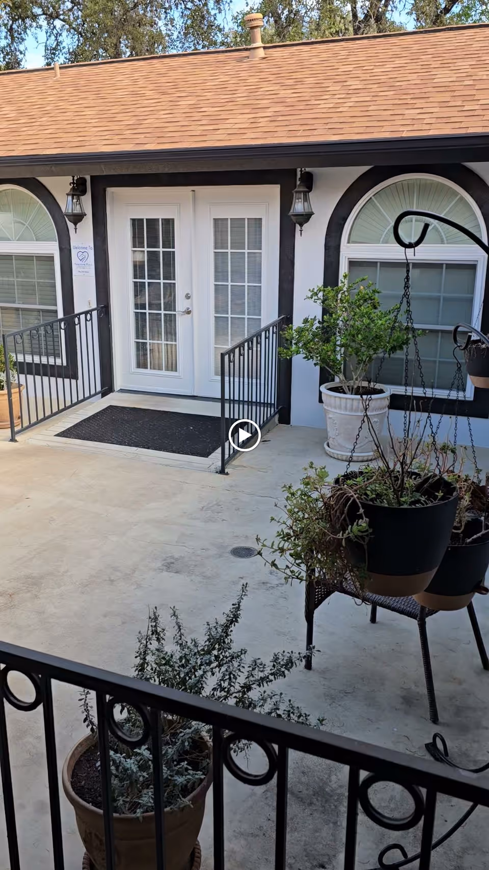Small courtyard with potted plants and a ramp leading to white double French doors of a single-story building.