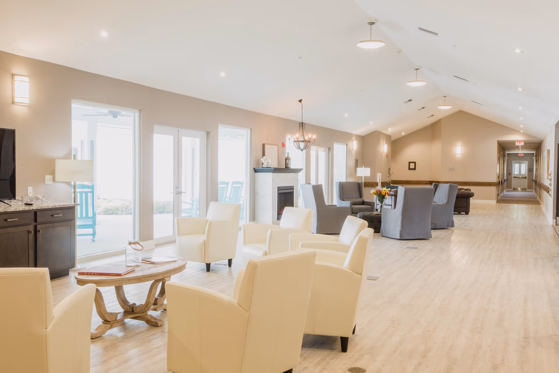 Bright, spacious communal lounge with cream and gray armchairs, coffee tables, and large windows/doors.