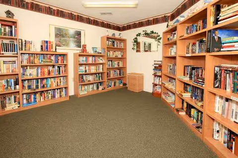 Interior library room with tall wooden bookshelves, green carpet, and wall artwork.