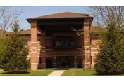 Brick building entrance with a covered portico, trees, and a walkway.