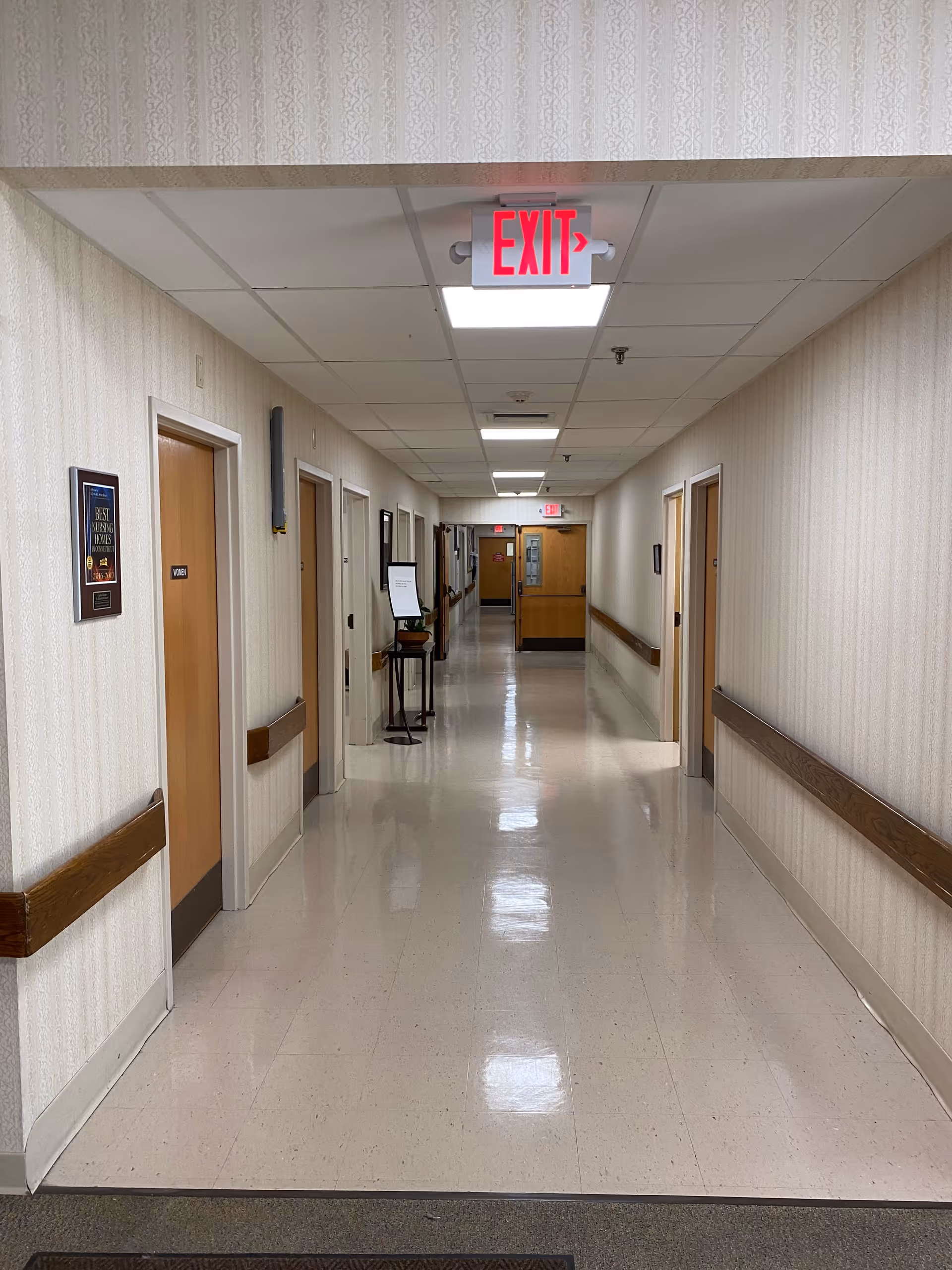 A long, polished interior hallway with doors, handrails and an illuminated EXIT sign at the ceiling.