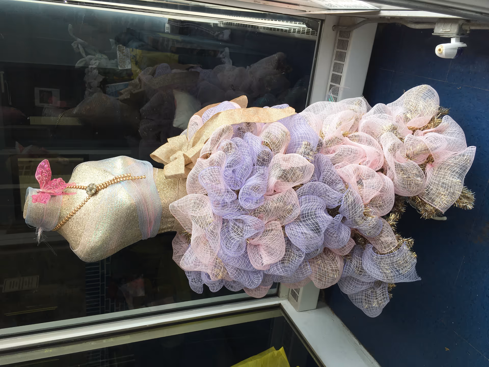 A decorative glittery dress form covered in pink and lavender mesh ribbons displayed indoors by a window.