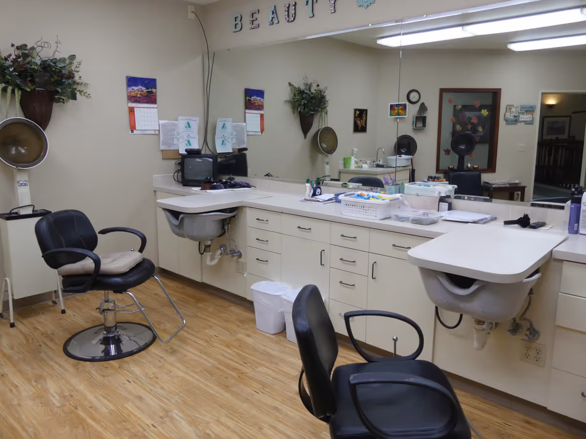 Interior beauty salon with styling chairs, wash basins, large mirror, and countertop cabinets.