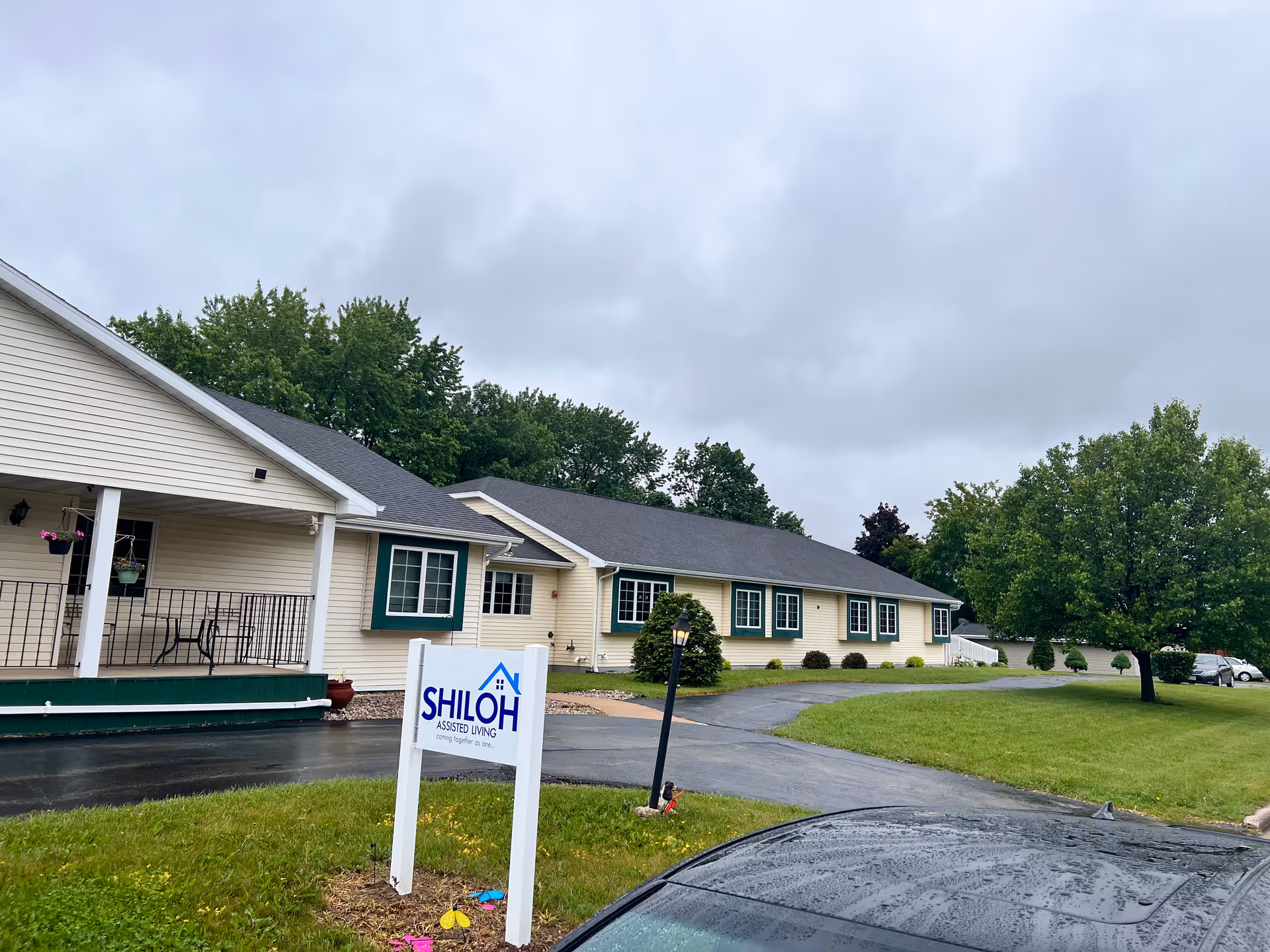 Front exterior of Shiloh Assisted Living single-story building with a driveway, lawn, and a sign in the foreground.