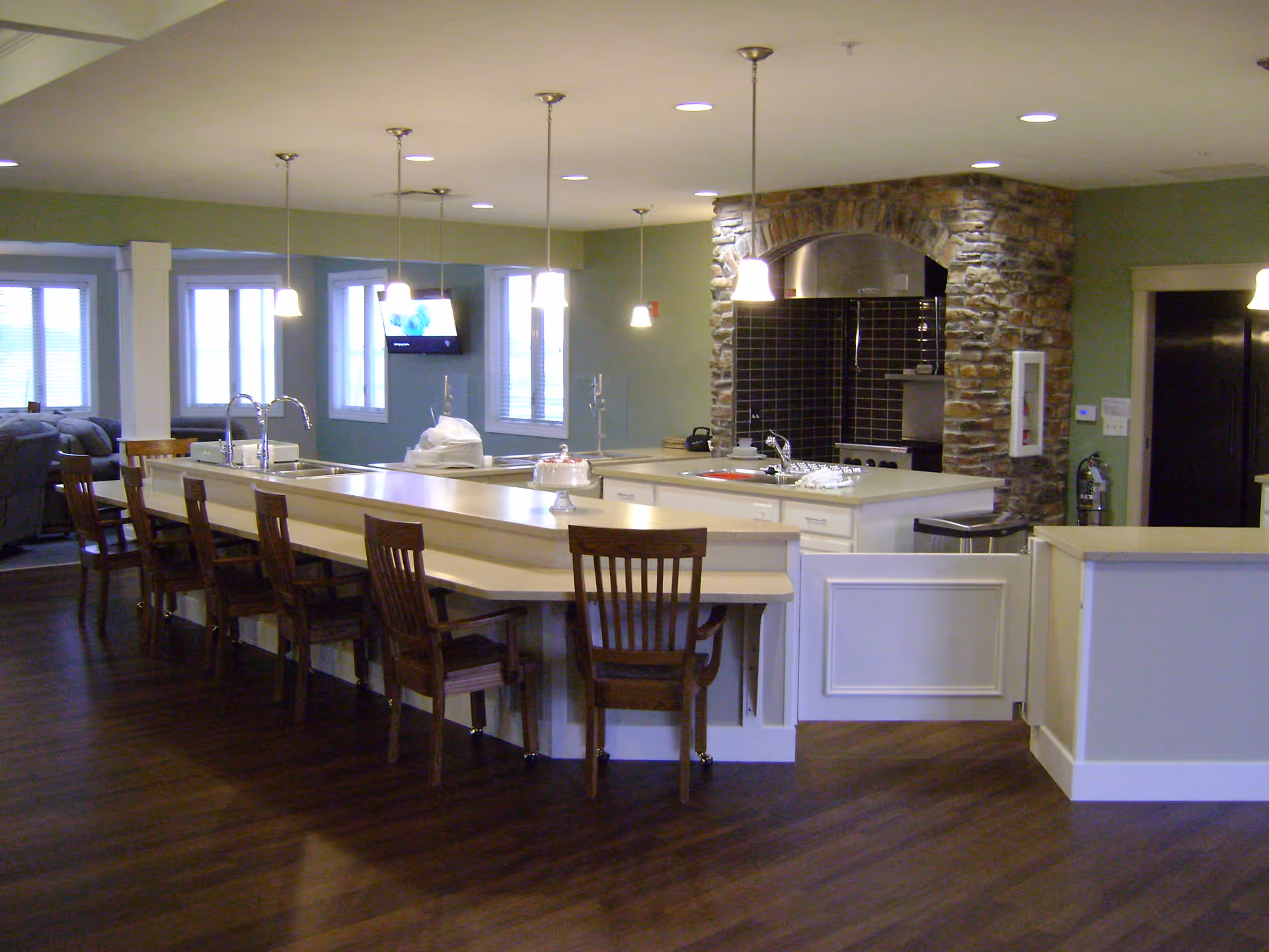 Open communal kitchen with a long center island, wooden bar chairs, pendant lights, and a stone-clad cooking area.