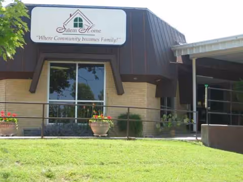 Exterior view of Salem Home facility with sign, entrance, and potted plants near the doorway