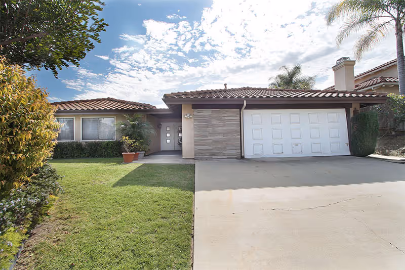 Front exterior of a single-story home with a tiled roof, two-car garage, driveway and manicured lawn.