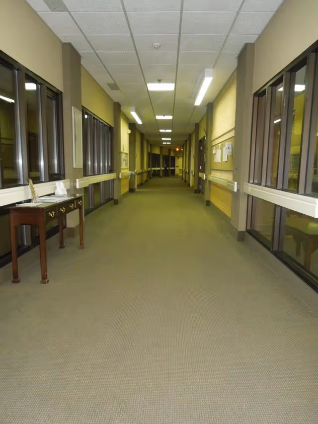 Long carpeted interior hallway with handrails and windows on both sides leading to distant doors.