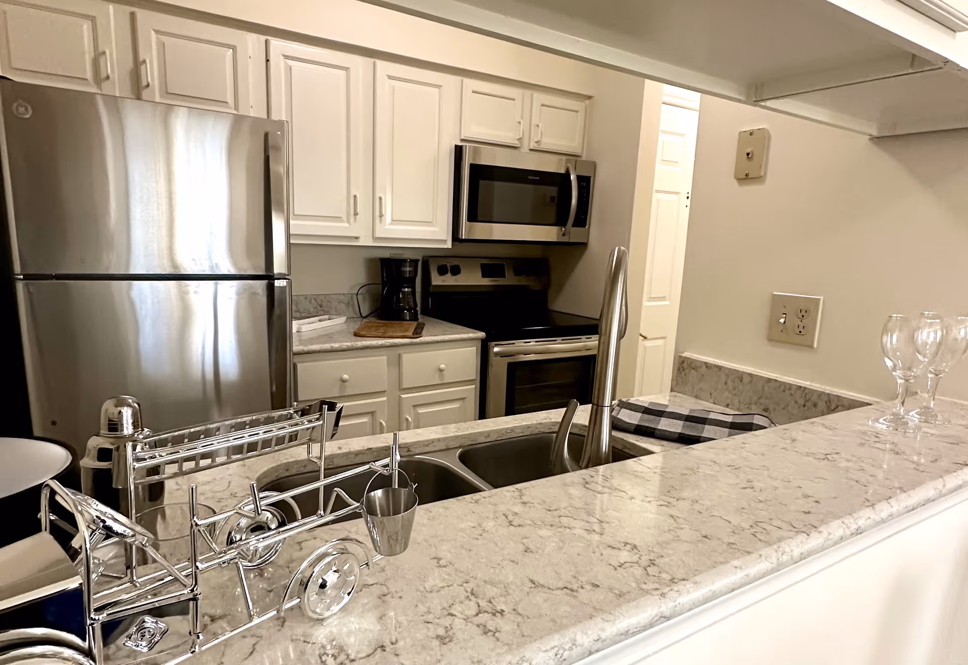 Open kitchen with a marble countertop, stainless steel refrigerator, sink, microwave and stove.