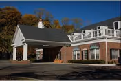 Exterior view of a brick building with white trim and a covered entrance driveway under a clear blue sky, surrounded by trees with autumn foliage.