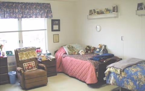 Cozy shared bedroom in a senior living facility with two beds and a chair.