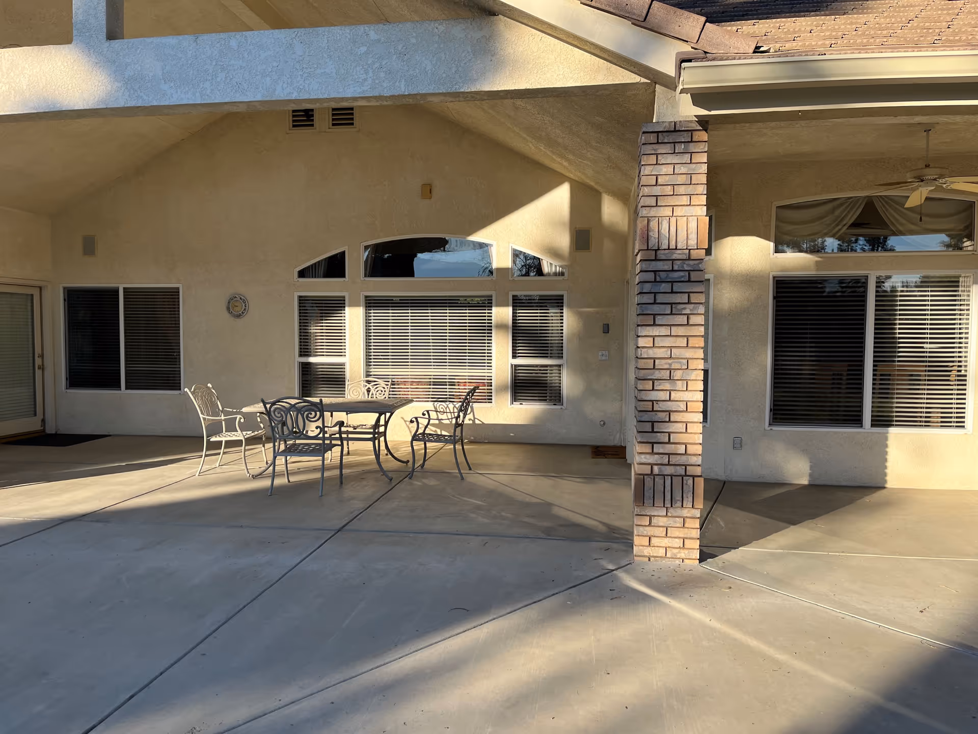 Covered outdoor patio with a metal table and chairs, a brick column, and windows with blinds.