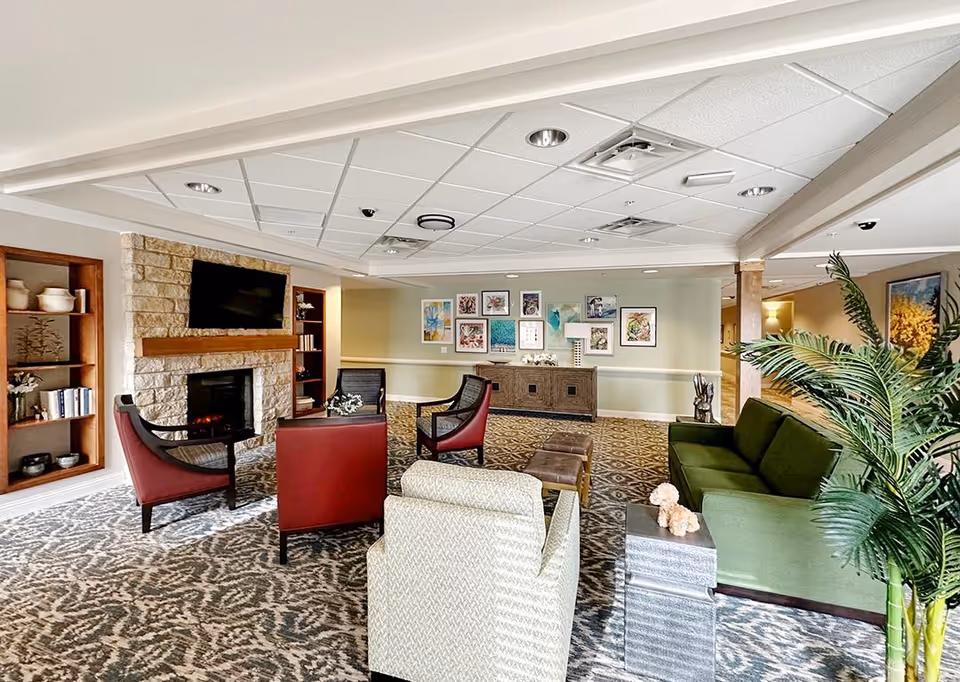 A cozy common room with sofas and armchairs arranged around a stone fireplace and wall-mounted TV.