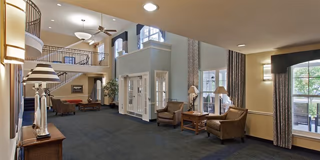 Spacious senior living lobby with high ceilings, balcony, seating areas, and large windows.