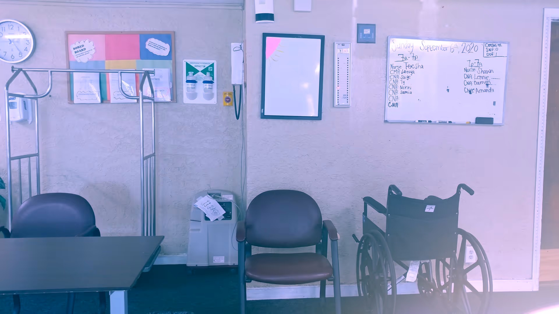 Interior common area with chairs, a wheelchair, an oxygen concentrator, and bulletin/whiteboards on the wall.