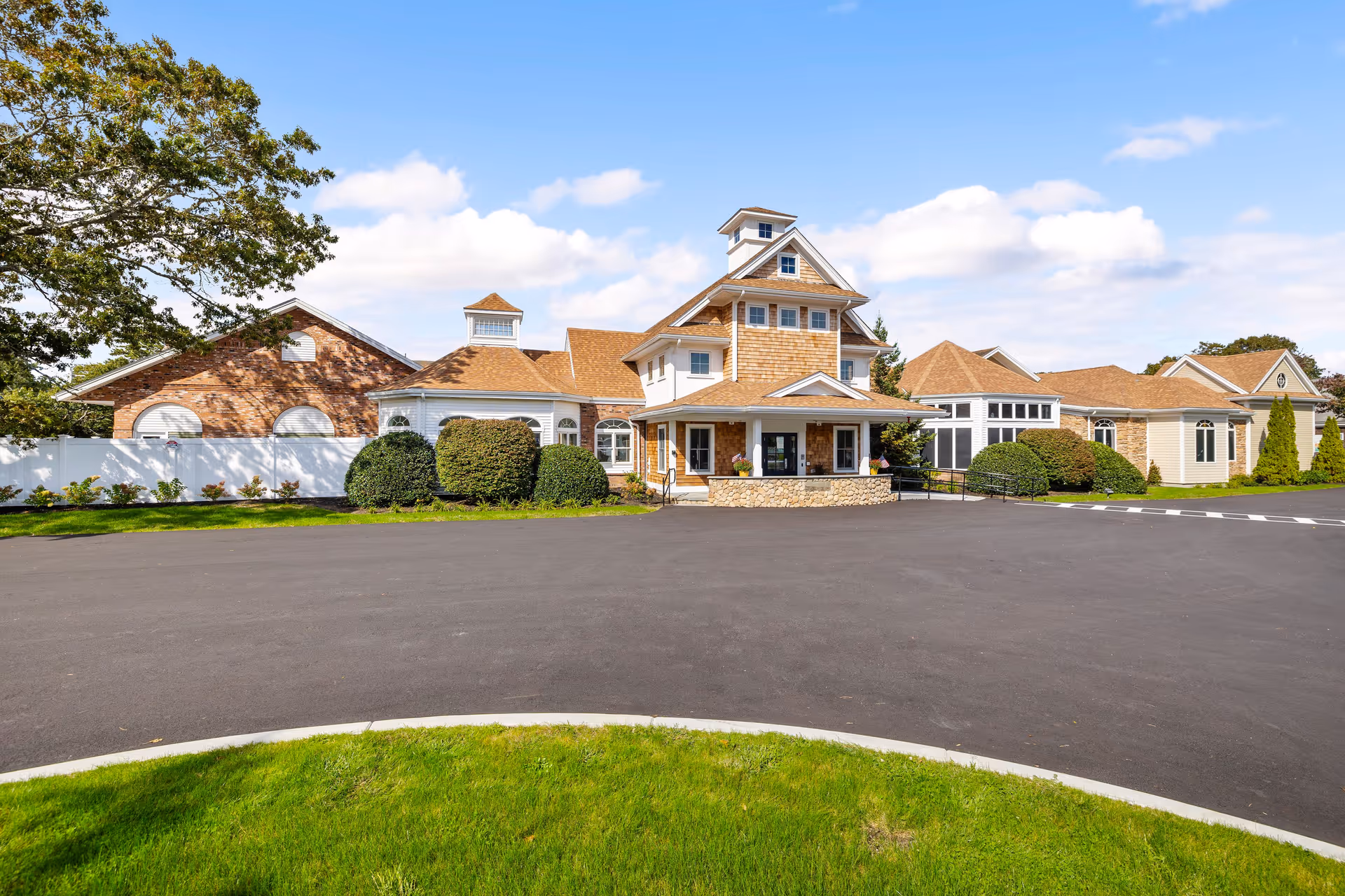 Front exterior of a residential senior living building with a central tower, covered entrance, landscaped shrubs, and a paved driveway.