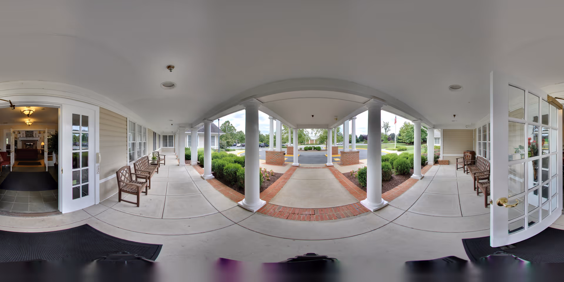 Covered front entry porch with white columns, benches, glass doors and a drive-up drop-off area at a senior living facility.