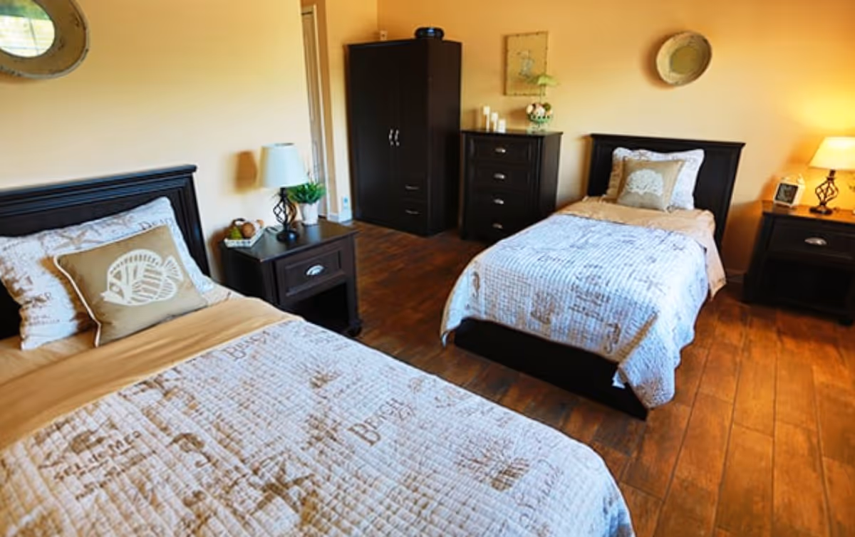 Two-bed furnished bedroom with dark wood furniture, nightstands, lamps, and hardwood floors.