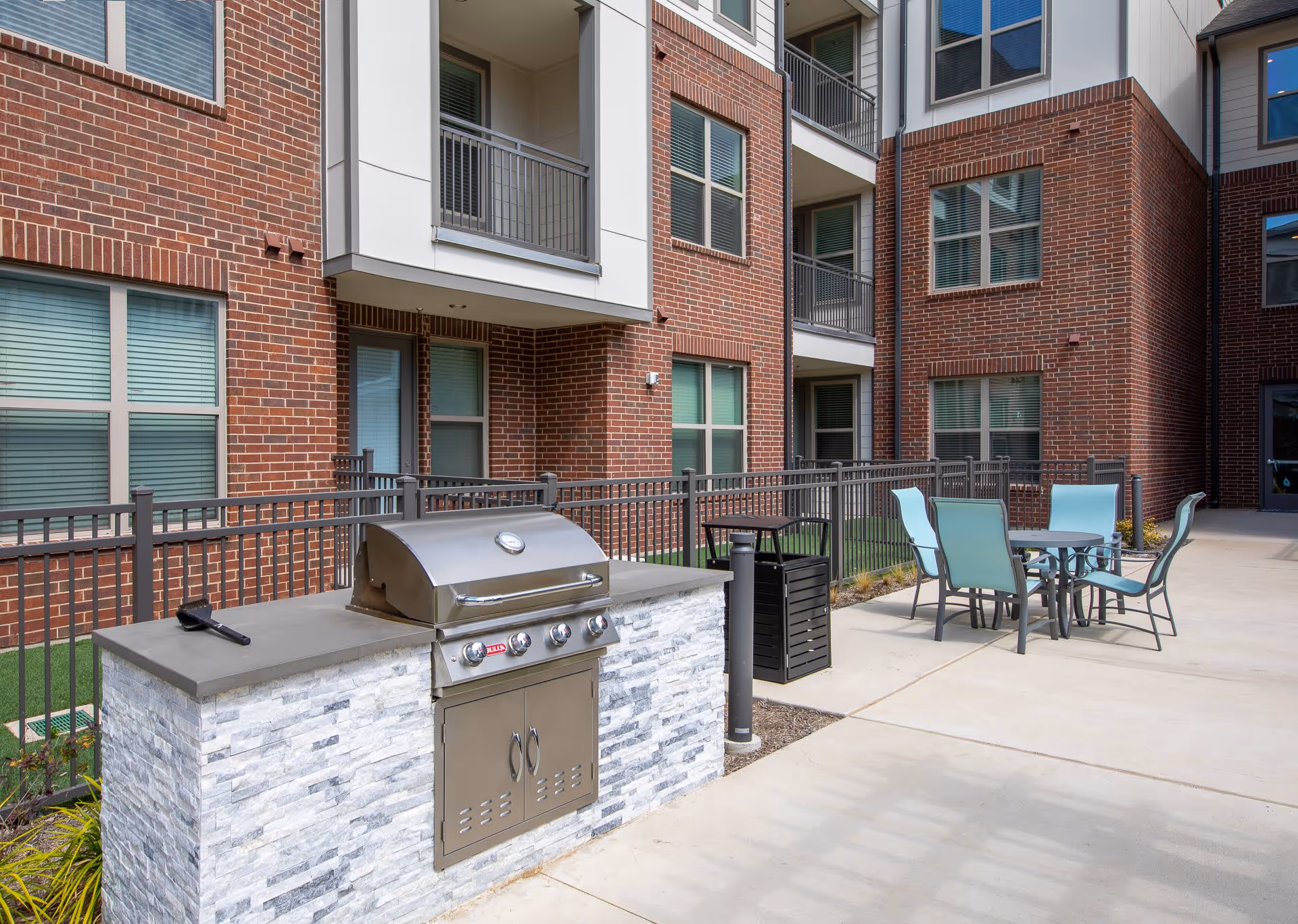 Outdoor courtyard of a brick apartment building with a built-in stainless steel grill and a patio table and chairs.