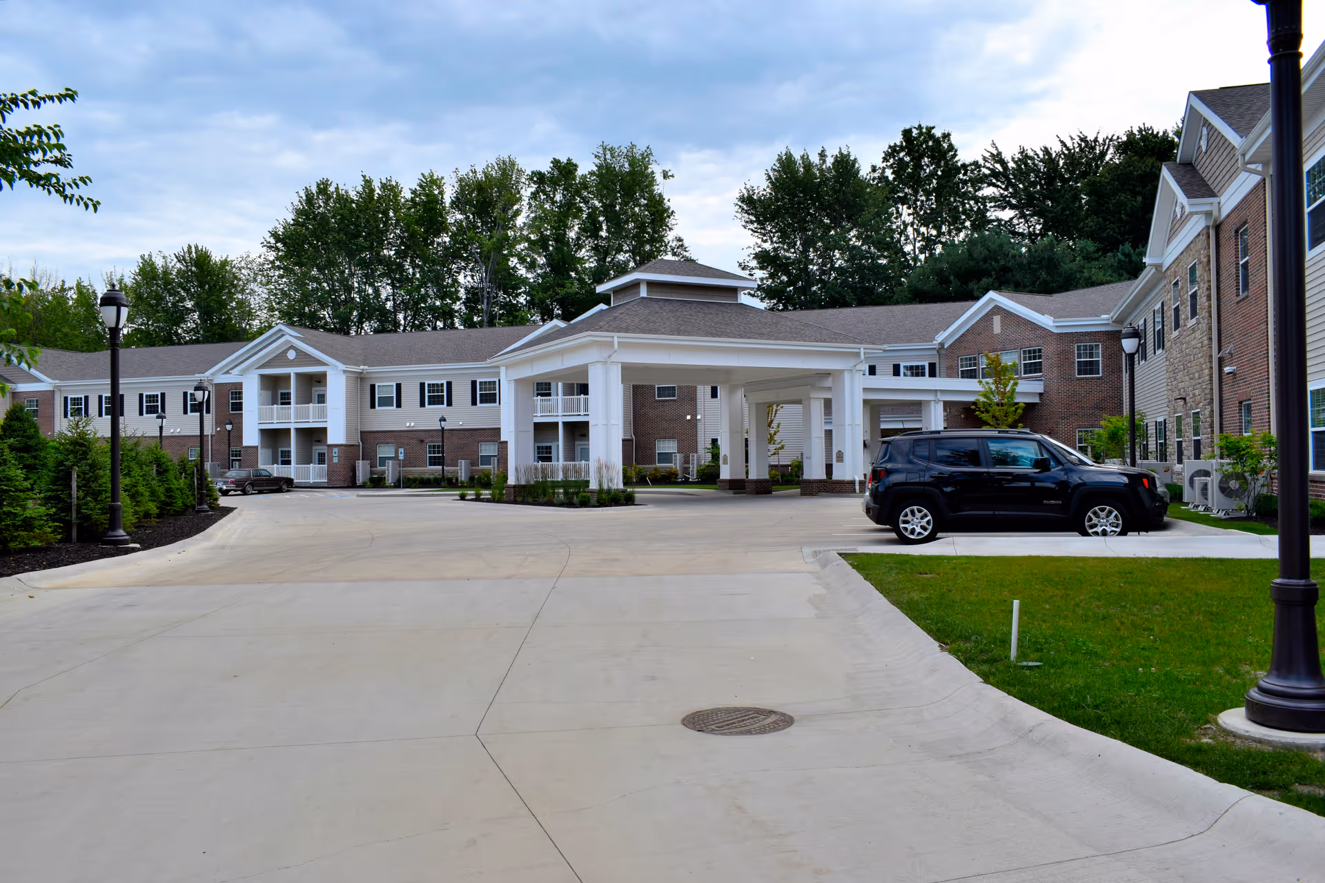 Exterior view of Danbury Mentor senior living facility with driveway, entrance canopy, and parked car.