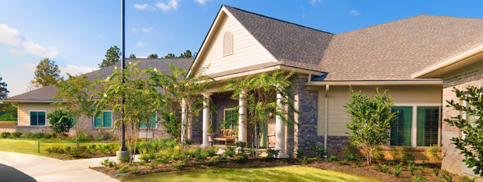 Single-story brick and siding senior living building with a covered columned entrance and landscaped front lawn.