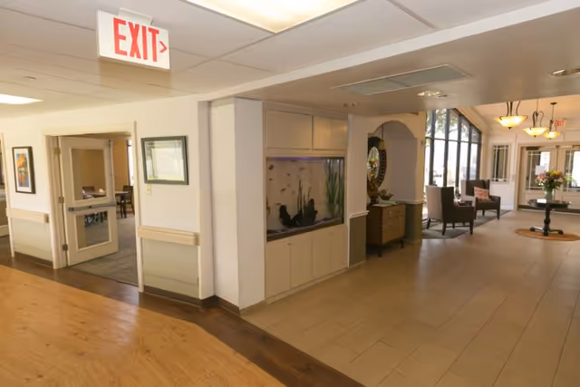 Lobby interior of a senior living facility with a built-in aquarium, seating area, and an exit sign overhead.