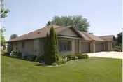 Single-story ranch-style building with three attached garages, landscaped lawn, and shrubs under a clear sky.