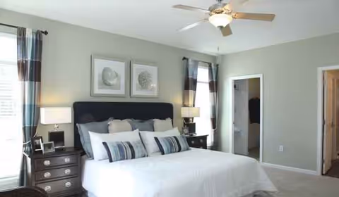A neatly made bedroom with a bed, upholstered headboard, two nightstands, lamps, and a ceiling fan.