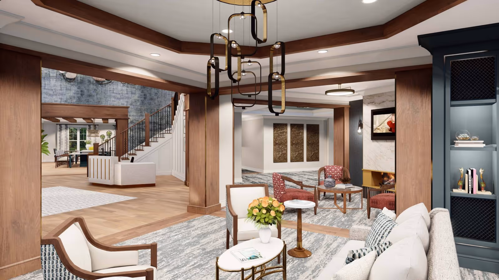 A spacious and elegantly furnished living room area in The Chelsea at West Orange, featuring comfortable seating including armchairs and a sofa, a coffee table with a vase of flowers, modern light fixtures hanging from the ceiling, and a fireplace with artwork above it. In the background, there is a staircase leading to an upper floor and a dining area with a table and chairs near large windows.
