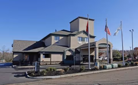 Facade of Prosperity Pointe senior living facility with entrance, flagpoles, and parking.