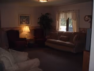 Cozy living room with sofa, armchairs, lamp, plant, and window with curtains.