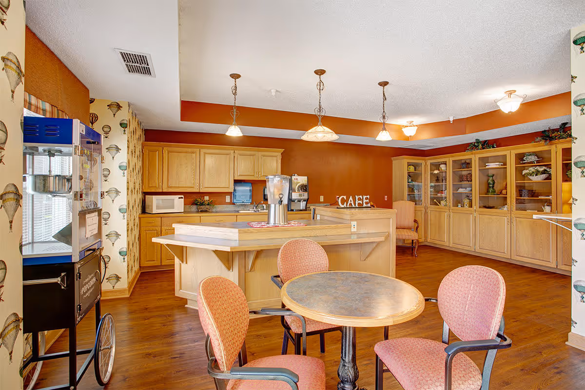 Café-style community dining area showing a round table with chairs, a central service island, a popcorn machine, and wooden cabinetry.
