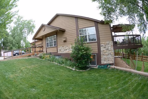 Single-story tan building with stone accents, a wheelchair ramp and deck, surrounded by a green lawn and trees.