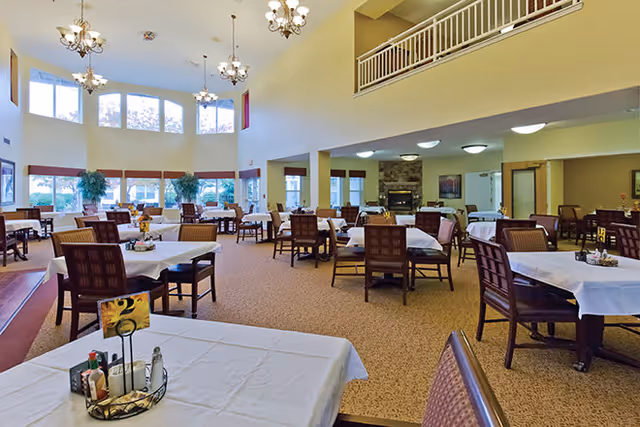 Spacious dining room with multiple tables and chairs, high ceilings, chandeliers, and large windows.