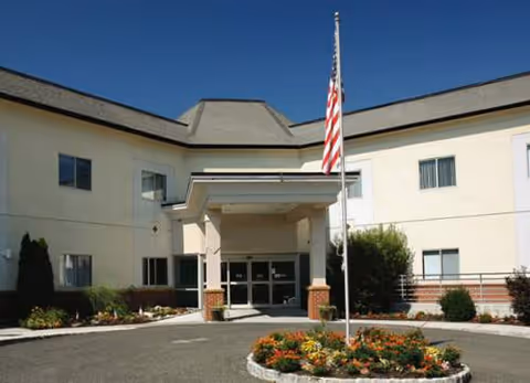 Front exterior view of Atrium Post Acute Care of Park Ridge entrance with flag and landscaping.