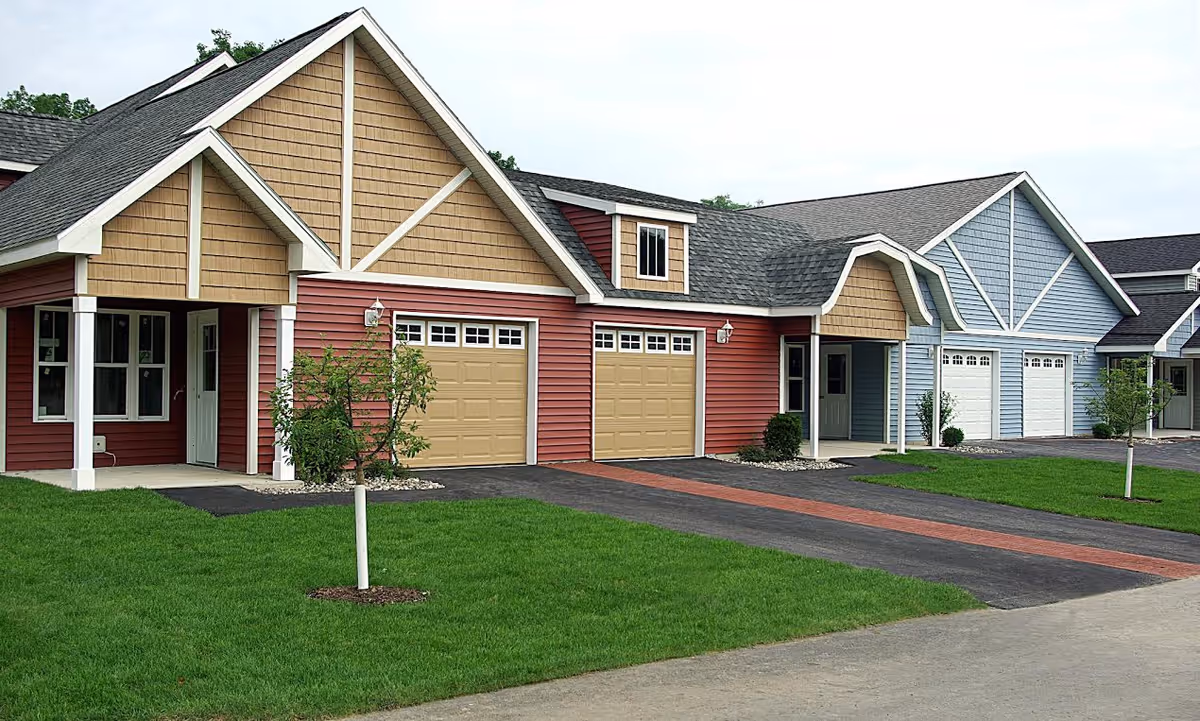Front view of attached single-story residential units with garages, porches, and manicured lawns.