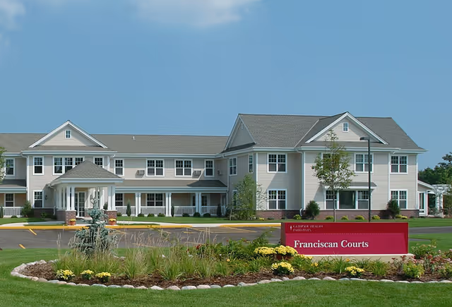 Exterior view of Franciscan Courts senior living facility with landscaped entrance and sign.