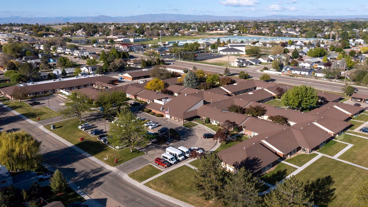 Aerial view of Sunny Ridge senior living campus showing connected brown-roof buildings, lawns, parking lot, and surrounding neighborhood.