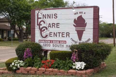 Exterior sign for Ennis Care Center with blooming flowers and landscaped bushes
