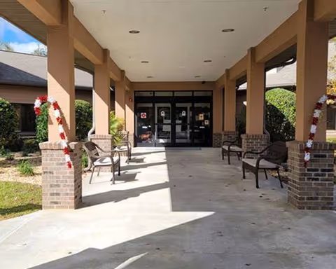 Covered entrance area of a building with brick pillars decorated with candy cane striped garlands, several benches along the sides, and glass double doors at the far end.