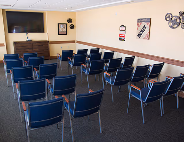 Small media/activity room with rows of blue chairs facing a large flat-screen TV and movie-themed wall decor.