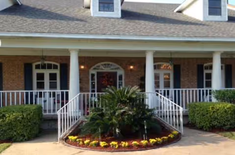 Front entrance of a brick senior living facility with columns and a circular flower bed.