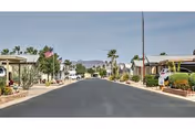 A wide paved road lined with desert landscaping, palm trees, and single-story buildings on both sides under a clear sky with mountains in the background.