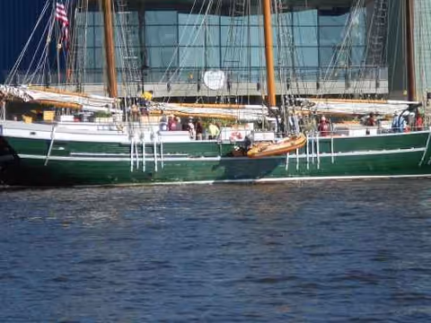 A green sailboat docked beside a glass-front building along the water.