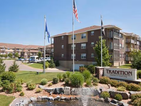 Exterior view of Tradition senior living building with flagpoles, landscaping, and fountain