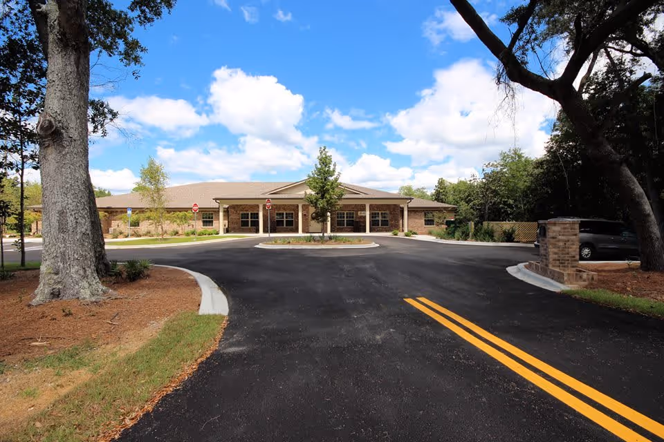 Front driveway and entrance of a single-story assisted living building with trees and a blue sky.