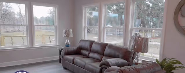 Bright living room with large windows, two brown leather sofas, side tables and lamps.